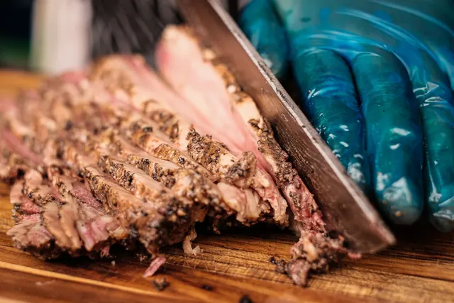 Smoked brisket being sliced on a board, first angle.