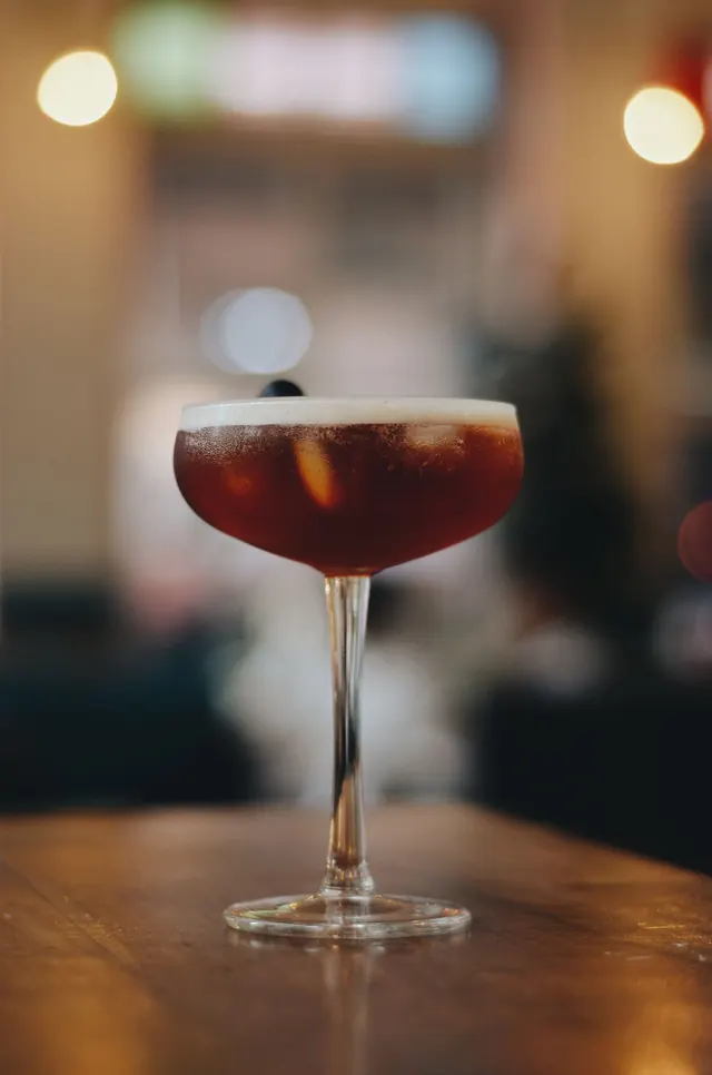 A dark cocktail in a coupe glass at a bar.