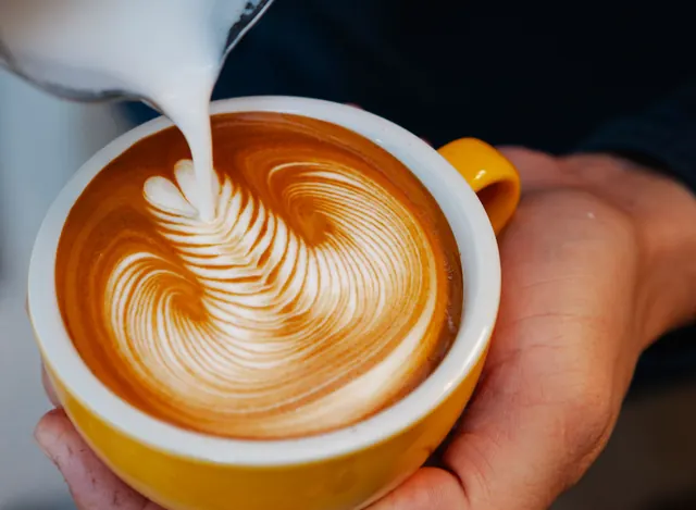 Latte art being poured into a yellow cup.