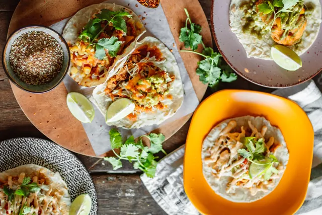 Taco platter with cilantro and lime on a wooden board.