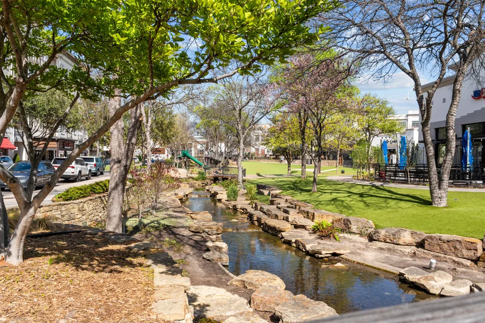 Trees and a waterway beside an outdoor retail area in Allen.