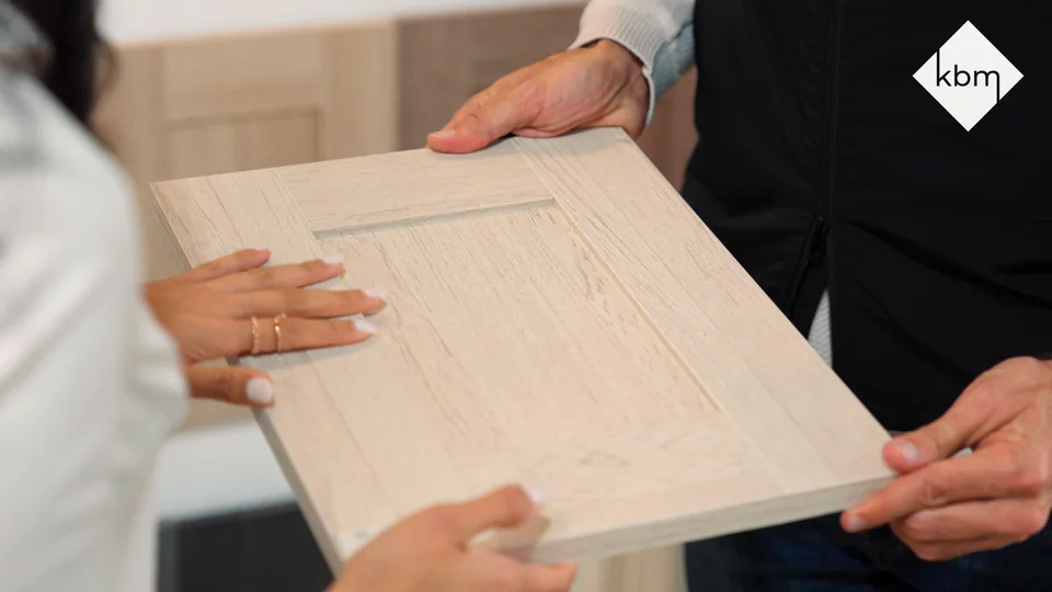 Hands hold a light wood cabinet-door sample.