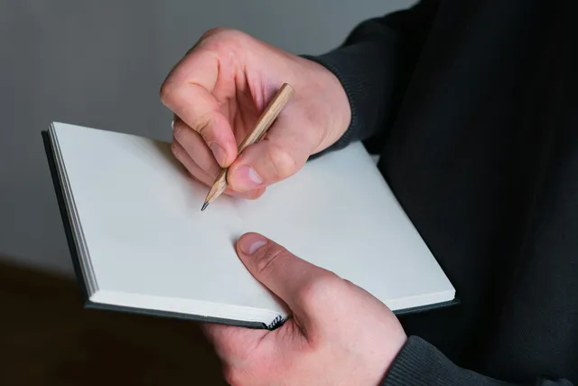 Hands hold a pencil above an open planning notebook.