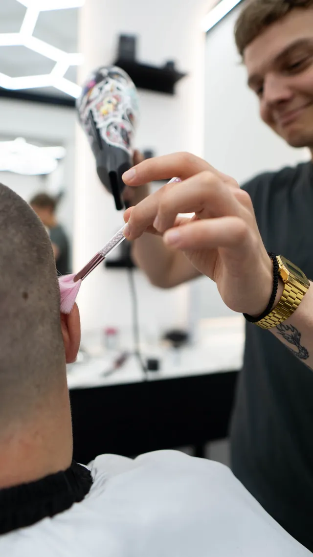 A barber uses a small brush to finish around the ear.