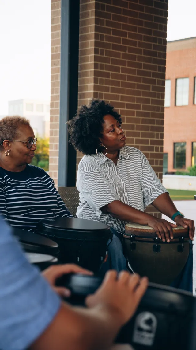 People sharing a group drumming session on a covered patio.