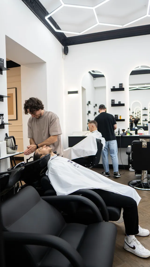 A barber rinses a customer’s hair at a salon wash basin.