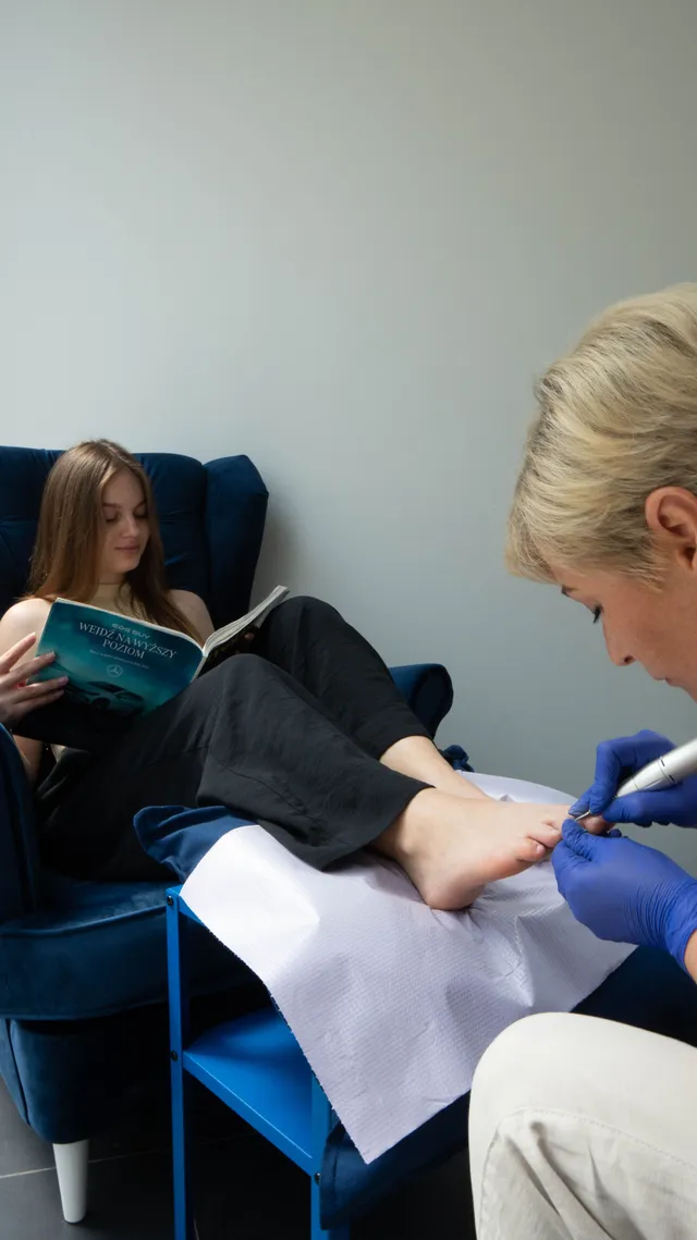 A nail technician works with a customer seated in a salon chair.