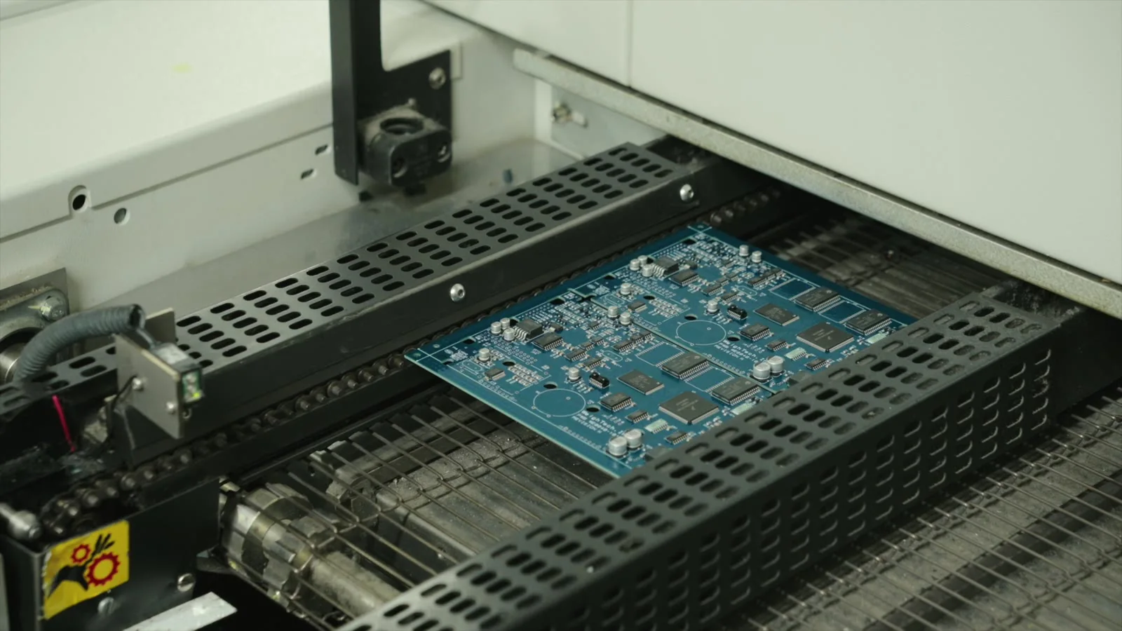 A circuit board moving through industrial machinery.