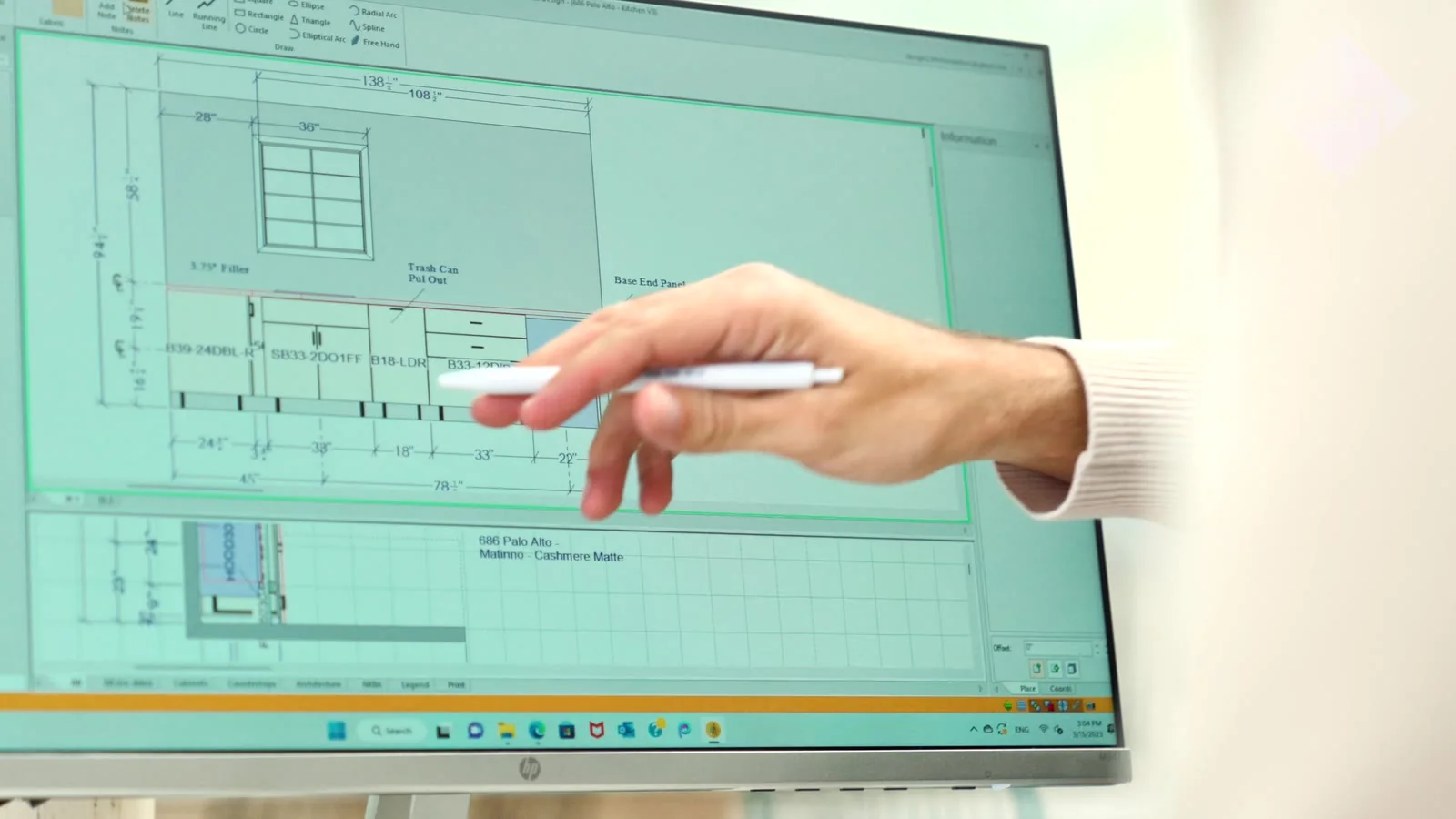 A hand pointing at cabinet design drawings.