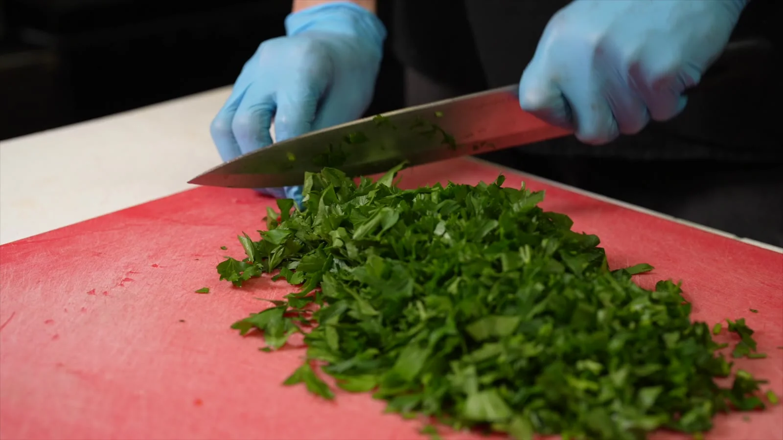 Gloved hands chopping herbs in a commercial kitchen.